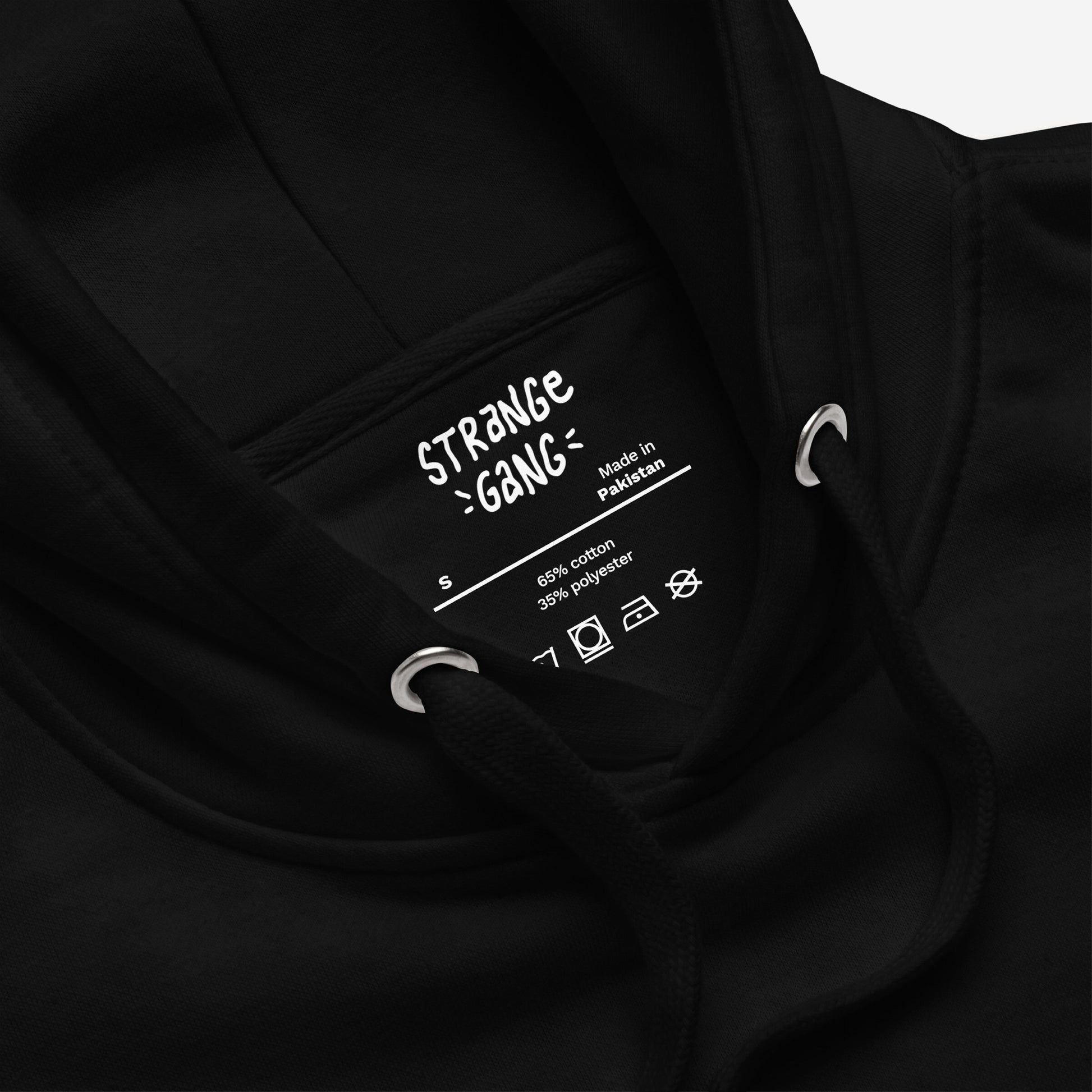 ICE Is State Sponsored Terrorism Hoodie: Close-up of neck area showing label details, including Made in Pakistan, size S, fabric content, and garment-care symbols, with black drawcords and metal eyelets visible.