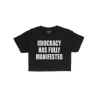 Idiocracy Women's Baby Tee features bold white text IDIOCRACY HAS FULLY MANIFESTED on a black T-shirt, highlighting societal 