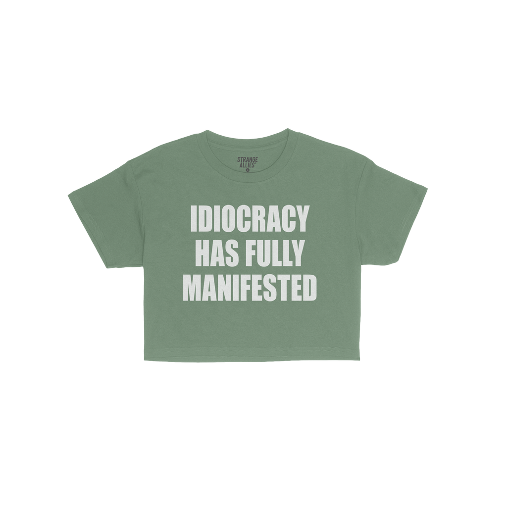The Idiocracy Women's Baby Tee features bold white text declaring “IDIOCRACY HAS FULLY MANIFESTED.”, capturing societal s