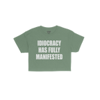 The Idiocracy Women's Baby Tee features bold white text declaring “IDIOCRACY HAS FULLY MANIFESTED.”, capturing societal s