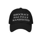 Black baseball-style cap featuring the bold embroidered text IDIOCRACY HAS FULLY MANIFESTED in classic serif type, blending s