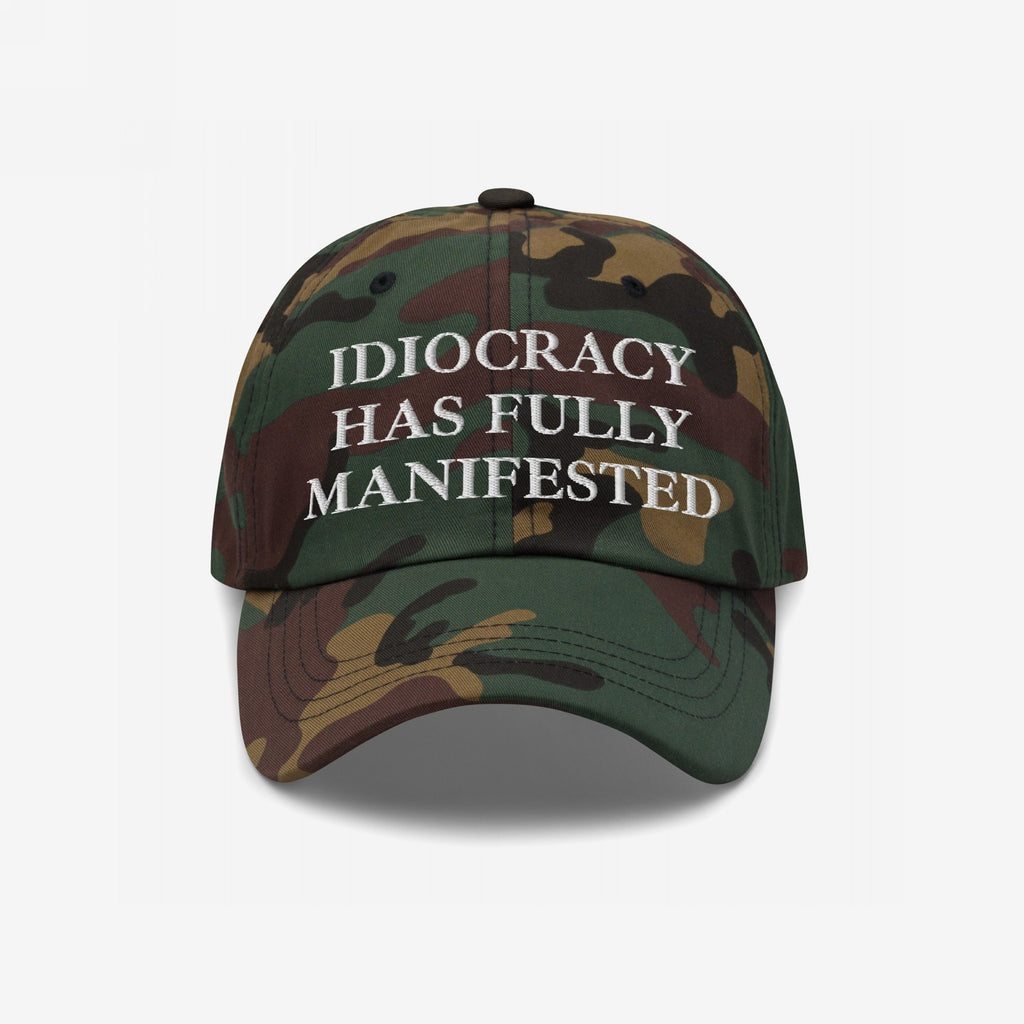 Camouflage-patterned Idiocracy Hat with white embroidered text declaring, IDIOCRACY HAS FULLY MANIFESTED, offering bold social commentary. Ideal for those who embrace provocative, thought-provoking statements through fashion.