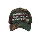 Camouflage-patterned Idiocracy Hat with white embroidered text declaring, IDIOCRACY HAS FULLY MANIFESTED, offering bold socia