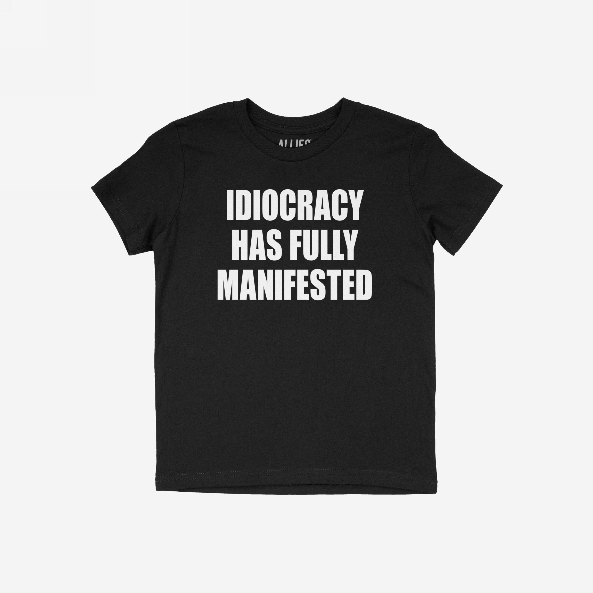 Black crew-neck T-shirt featuring the slogan IDIOCRACY HAS FULLY MANIFESTED in bold white letters, conveying a satirical and politically charged message.