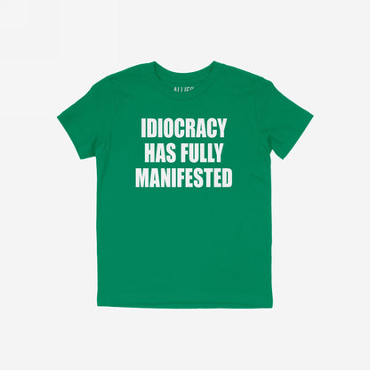 Green Idiocracy T-shirt with bold white text, “IDIOCRACY HAS FULLY MANIFESTED.”, reflecting a blunt statement for the politically disillusioned, embodying the spirit of resistance and truth with wit.