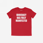 Red T-shirt with bold white text: IDIOCRACY HAS FULLY MANIFESTED. The Idiocracy T-shirt delivers a stark message, suited for those questioning modern realities, reflecting the store's socially conscious ethos.