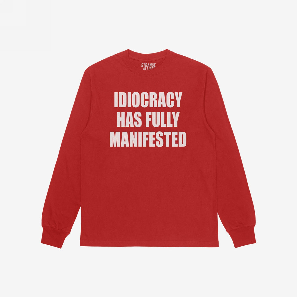 Idiocracy T-shirt in red with bold white slogan IDIOCRACY HAS FULLY MANIFESTED on the front, reflecting a sharp, satirical message. Label inside the collar reads STRANGE ALLIES.