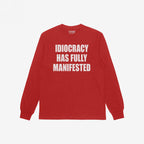 Idiocracy T-shirt in red with bold white slogan IDIOCRACY HAS FULLY MANIFESTED on the front, reflecting a sharp, satirical message. Label inside the collar reads STRANGE ALLIES.