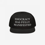 Black snap-back baseball cap with white serif text: “IDIOCRACY HAS FULLY MANIFESTED.” The Idiocracy Hat delivers bold social commentary, ideal for those who wear their beliefs front and center.