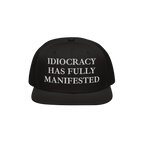 Black snap-back baseball cap with white serif text: “IDIOCRACY HAS FULLY MANIFESTED.” The Idiocracy Hat delivers bold soc