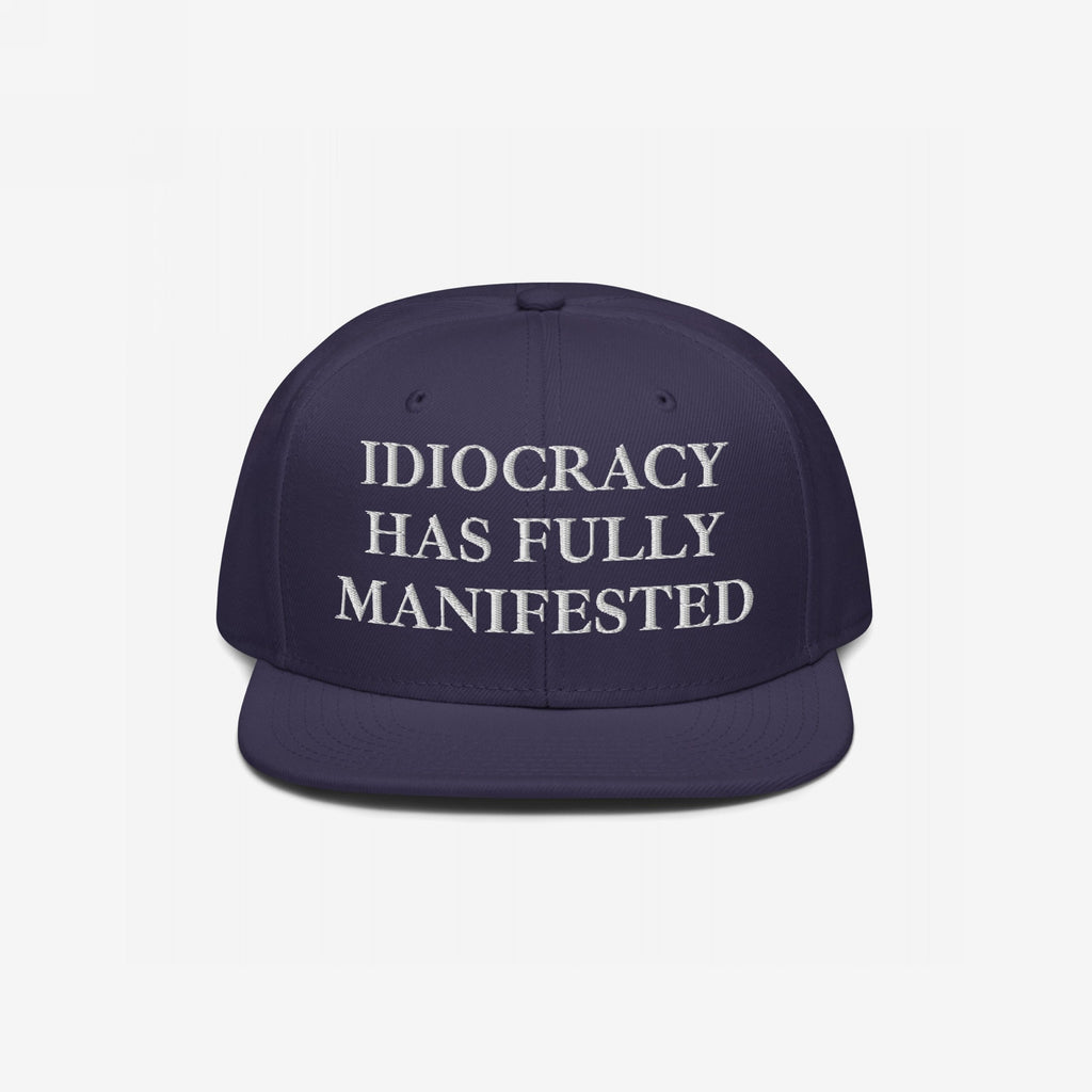 Dark-blue flat-brimmed Idiocracy Hat with white embroidered serif text: IDIOCRACY HAS FULLY MANIFESTED. A bold statement piece for those who embrace social commentary through fashion.