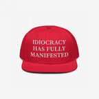 Bright-red Idiocracy Hat with white embroidered text, IDIOCRACY HAS FULLY MANIFESTED, in classic serif type, ideal for those expressing bold social commentary.