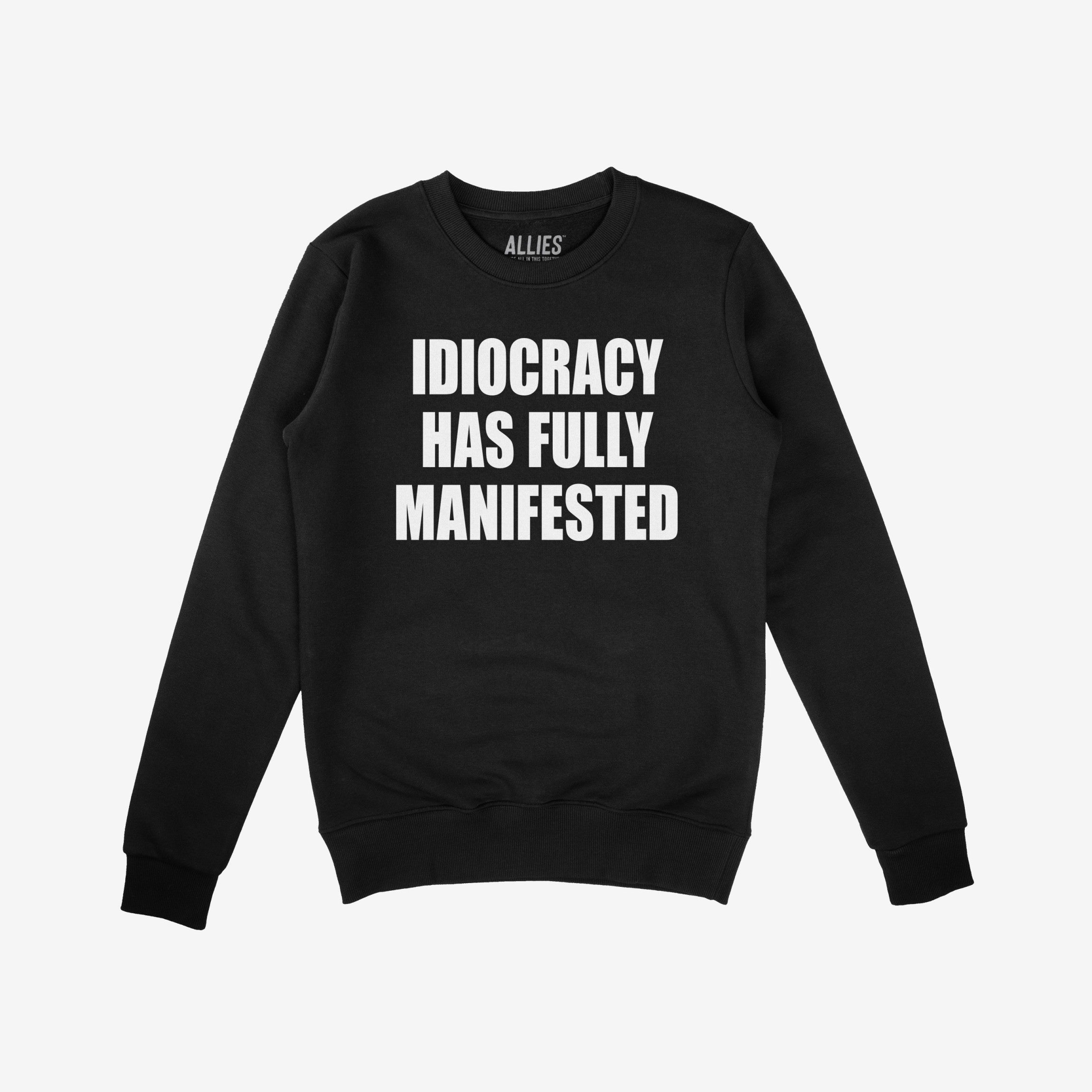 Black crewneck sweatshirt with bold white text reading IDIOCRACY HAS FULLY MANIFESTED, reflecting a political statement. Brand ALLIES. visible inside collar, aligning with anti-fascist, protest-themed apparel.