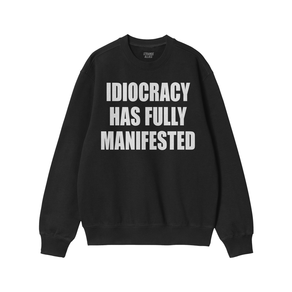 Black crewneck sweatshirt with bold white text reading IDIOCRACY HAS FULLY MANIFESTED, reflecting a political statement. Bran