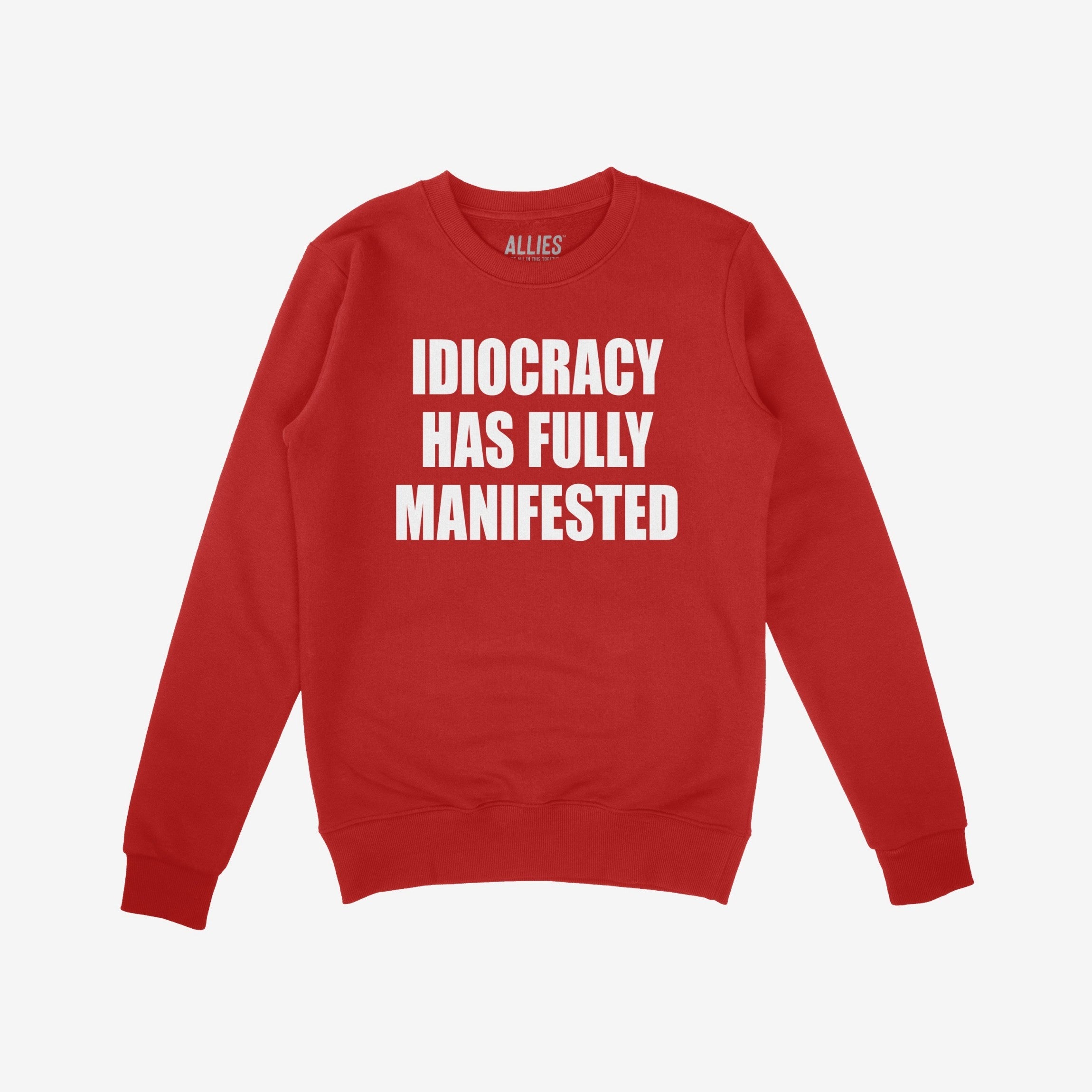 Red crewneck Idiocracy Sweatshirt with bold white text stating “IDIOCRACY HAS FULLY MANIFESTED,” echoing a protest against modern politics, designed for those challenging power. Label reads “ALLIES.”