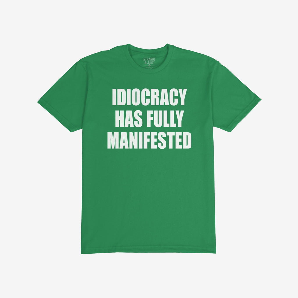 Green, short-sleeved Idiocracy T-shirt features bold white text stating “IDIOCRACY HAS FULLY MANIFESTED”, reflecting a satirical take on current events, ideal for the politically disillusioned and meme enthusiasts.