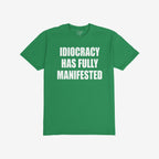 Green, short-sleeved Idiocracy T-shirt features bold white text stating “IDIOCRACY HAS FULLY MANIFESTED”, reflecting a satirical take on current events, ideal for the politically disillusioned and meme enthusiasts.
