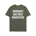 Green, short-sleeved Idiocracy T-shirt features bold white text stating “IDIOCRACY HAS FULLY MANIFESTED”, reflecting a sa