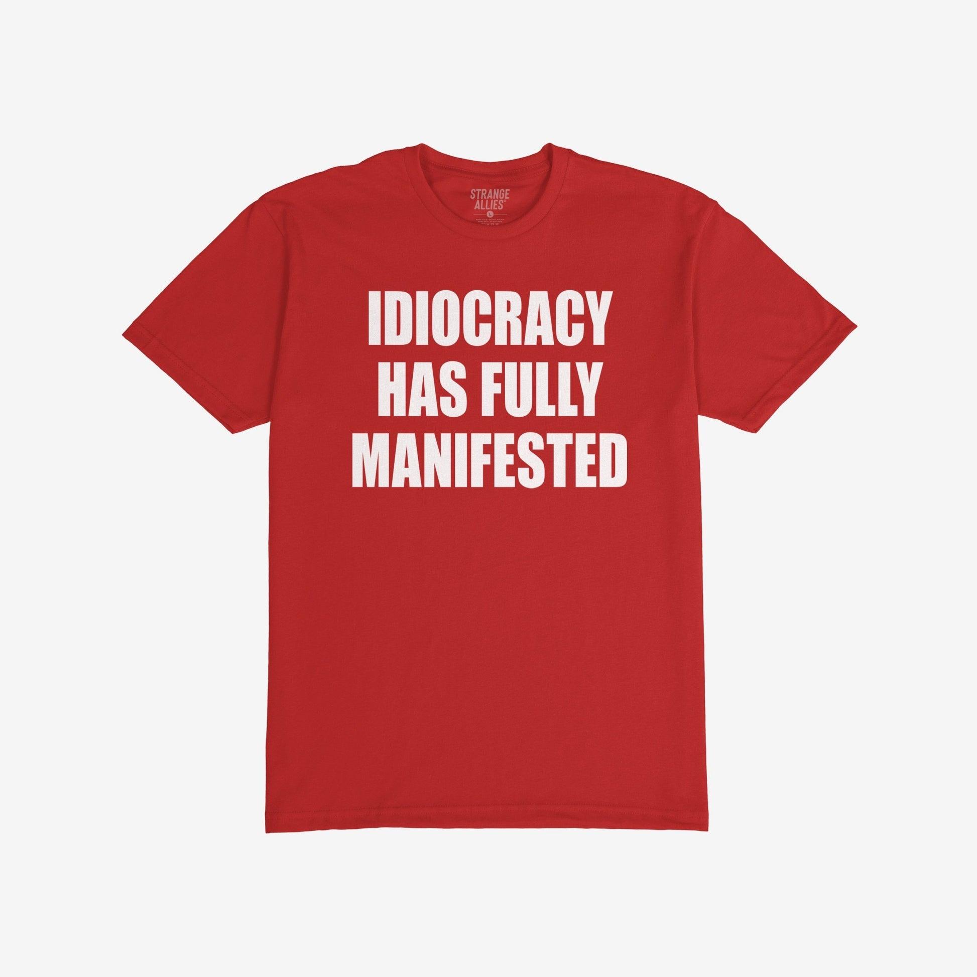 Idiocracy T-shirt with bold white text: IDIOCRACY HAS FULLY MANIFESTED. Brand label STRANGE ALLIES visible in collar. A statement piece for those embracing blunt truth and political commentary.