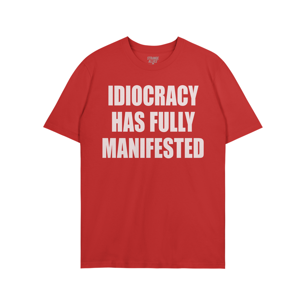 Idiocracy T-shirt with bold white text: IDIOCRACY HAS FULLY MANIFESTED. Brand label STRANGE ALLIES visible in collar. A state