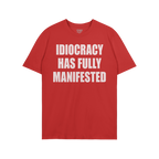 Idiocracy T-shirt with bold white text: IDIOCRACY HAS FULLY MANIFESTED. Brand label STRANGE ALLIES visible in collar. A state
