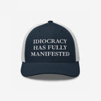 Navy-blue and white trucker-style cap with “IDIOCRACY HAS FULLY MANIFESTED” embroidered on the front, reflecting social commentary. Ideal for those who embrace bold statements with the Idiocracy Hat.