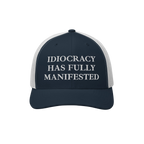 Navy-blue and white trucker-style cap with “IDIOCRACY HAS FULLY MANIFESTED” embroidered on the front, reflecting social c