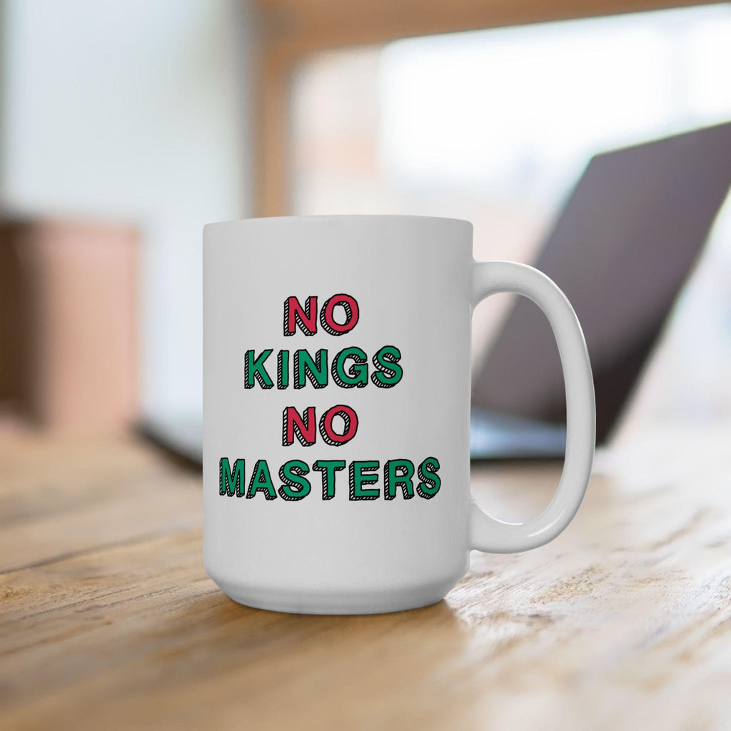 White ceramic No Kings No Masters Mug on a wooden tabletop, featuring bold hand-drawn text in contrasting colors. A laptop sits blurred in the background, suggesting a workspace setup.