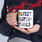 Person holds a Protect My LGBTQ+ Homies mug with rainbow letters, showcasing support and allyship. The holder wears a dark sweater with a red reindeer motif, embodying solidarity and festive spirit.