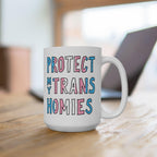 White ceramic Protect My Trans Homies Mug on a wooden table, featuring bold block letters filled with transgender pride colors, promoting equality and respect. Background shows a blurred laptop outline.