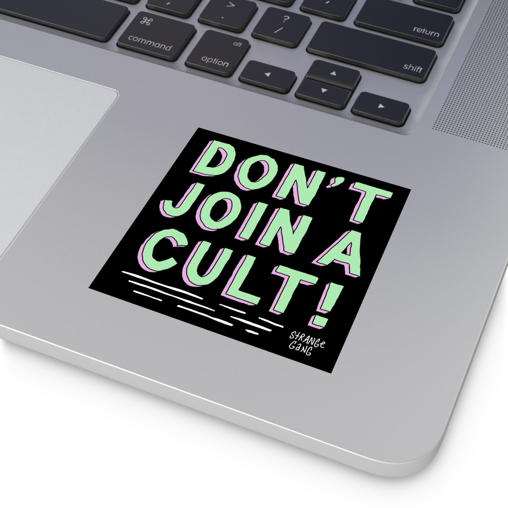 Corner of a silver laptop with a 'Don't Join A Cult' sticker beside the trackpad, featuring bold, hand-drawn letters. Ideal for promoting critical thinking and challenging authoritarian ideologies.