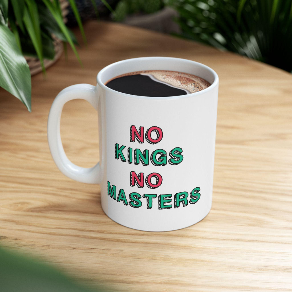 A white ceramic No Kings No Masters Mug on a wooden table, featuring a bold, hand-drawn slogan. It's filled with black coffee, embodying a rebellious spirit for those challenging authority.