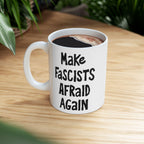 Make Fascists Afraid Again Mug on a wooden tabletop, featuring bold hand-lettered slogan. Filled with black coffee, this ceramic mug embodies resistance and activism, designed to inspire courage and defiance.