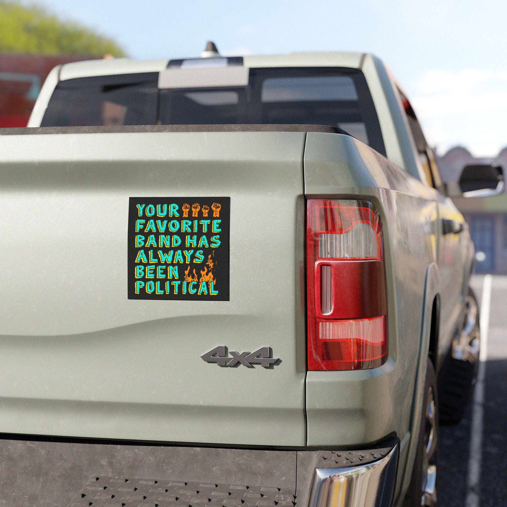 The rear of a 4x4 pickup displays the Your Favorite Band Has Always Been Political sticker, featuring raised-fist icons and flames, highlighting its weatherproof design for punk and progressive values.