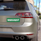Rear of a silver hatchback displaying an IMMIGRANT sticker with distressed lettering. This vinyl sticker embodies resilience and pride, perfect for showcasing support for the immigrant story on vehicles and more.