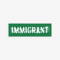 Aerial view of a street scene with a green banner reading IMMIGRANT in white, jagged letters over barbed-wire graphics. Immigrant Sticker & Magnet symbolizes unity and resilience against anti-immigrant sentiment.