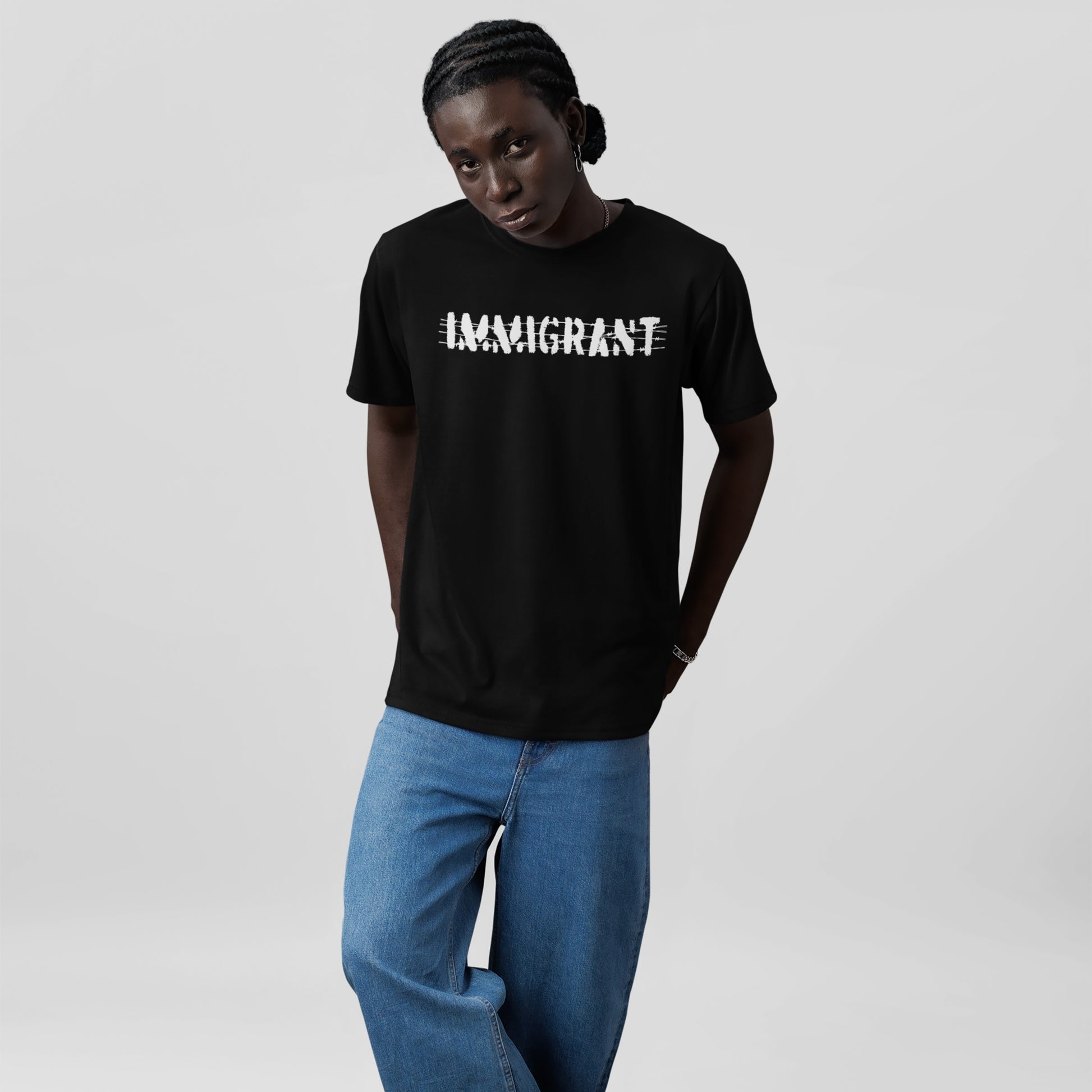 Young Black man models the Immigrant Shirt featuring distressed IMMIGRANT lettering, expressing resilience and unity. Styled with cornrow braids and accessories, it embodies activism and solidarity.