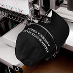 Multi-head embroidery machine stitching IMMIGRANTS MAKE AMERICA GREAT onto a black baseball cap. The cap, secured by an embroidery hoop, features a CLASSIC swing-tag on its adjustable strap.