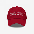 Red baseball-style cap featuring white embroidered text: IMMIGRANTS MAKE AMERICA GREAT. This statement piece supports immigrant communities, aligning with anti-racism and equality values. Benefiting the Immigrant Legal Resource Center (ILRC).