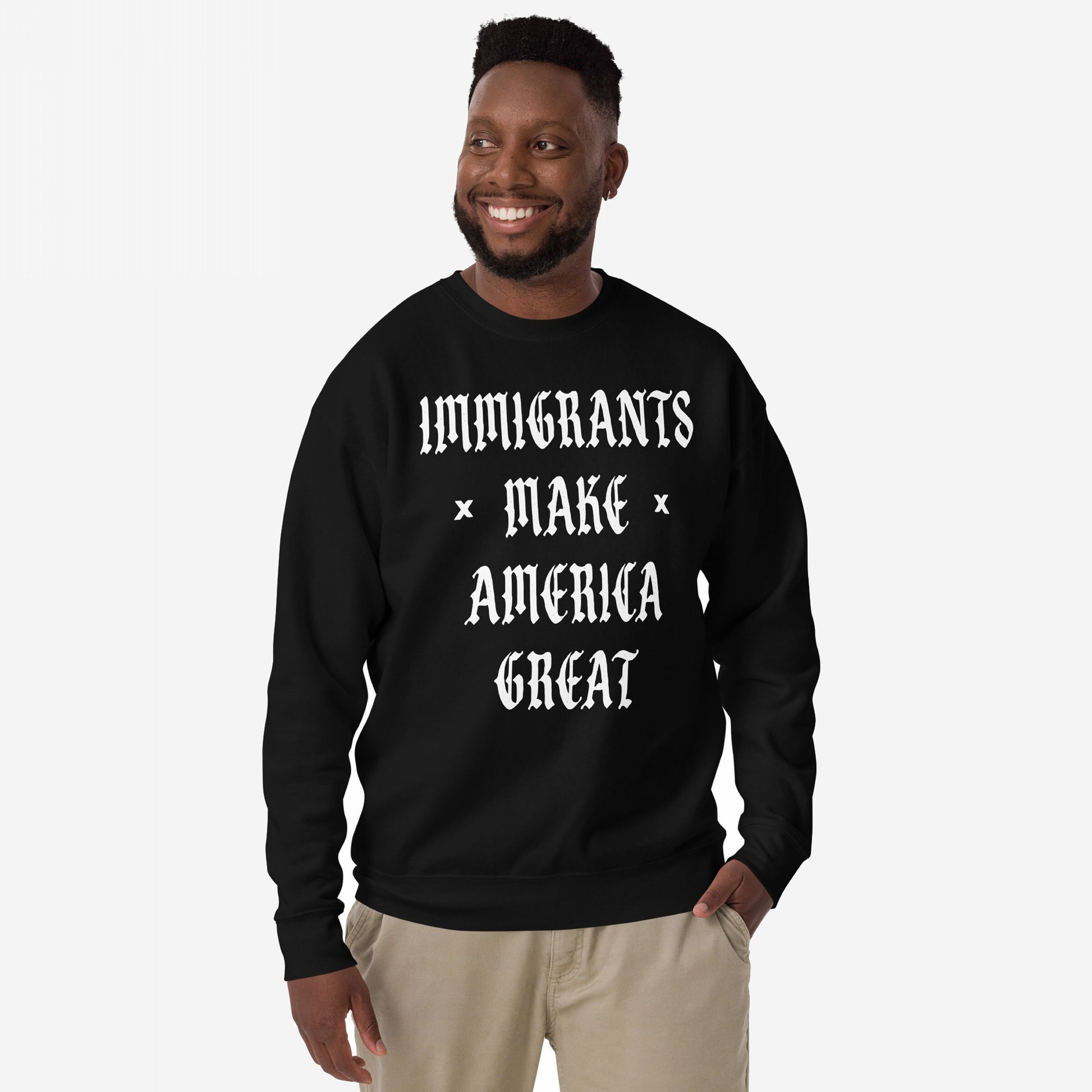 Smiling man models the Immigrants Make America Great Sweatshirt featuring bold white Old English text, advocating for immigrant pride and protest against racism and nationalism.