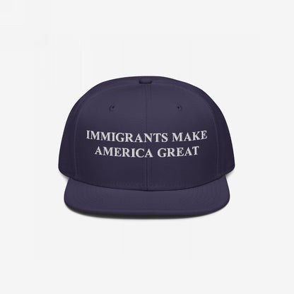Navy-blue flat-brimmed cap with bold white embroidery reading “IMMIGRANTS MAKE AMERICA GREAT,” symbolizing resilient stance for immigrant rights, perfect for rallies or everyday wear, supporting Amnesty International.