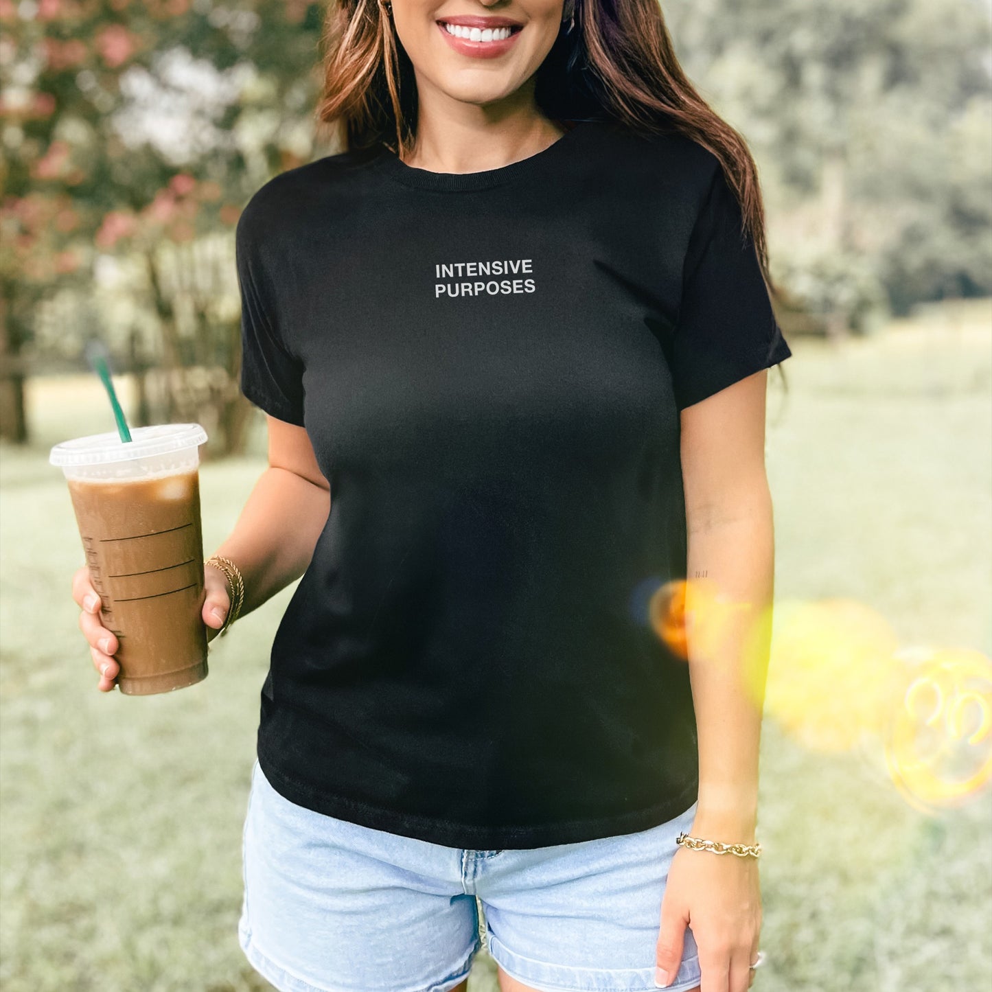 Intensive Purposes Women's Baby Tee features boldly on a smiling person outdoors, paired with denim shorts and a gold bracelet, capturing sunlight and chaos energy in its minimalist design.