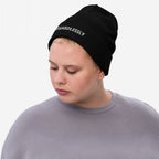 Person wearing the Irregardlessly Hat, a black knit beanie with REGARDLESSLY embroidered on the cuff, embodying a playful defiance against grammar norms. They're dressed simply, focusing on the bold statement accessory.