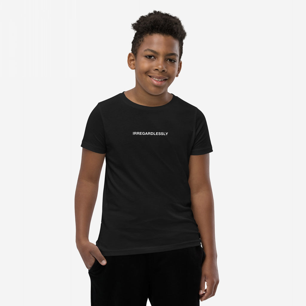 Smiling boy wearing the Irregardlessly T-shirt, featuring the word IRREGARDLESSLY on a fitted black tee. His left hand rests in his pocket, embodying playful defiance and irony.
