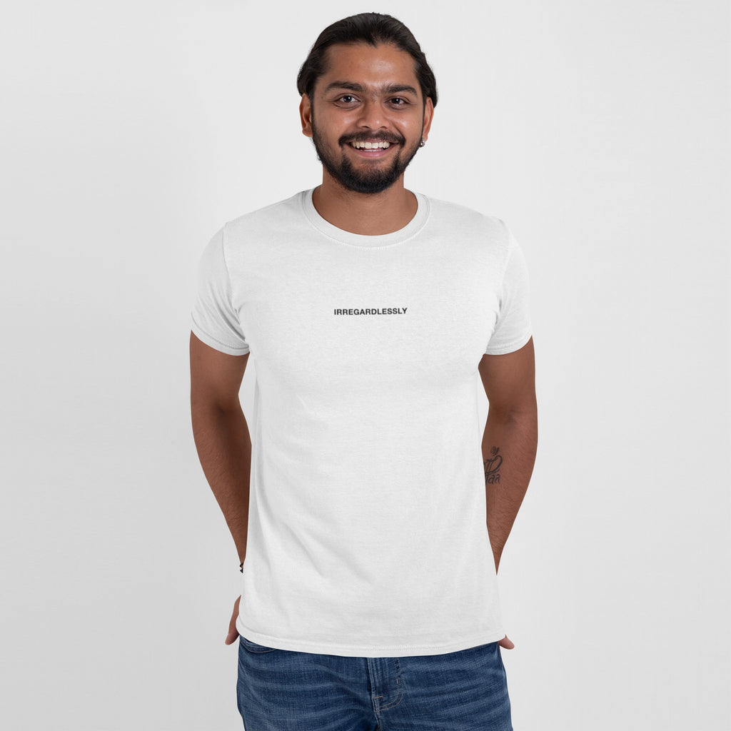 Man in white Irregardlessly T-shirt smiles at the camera. The design playfully subverts grammar, appealing to fans of ironic humor and unconventional expressions. Casual jeans and forearm tattoo complete the look.