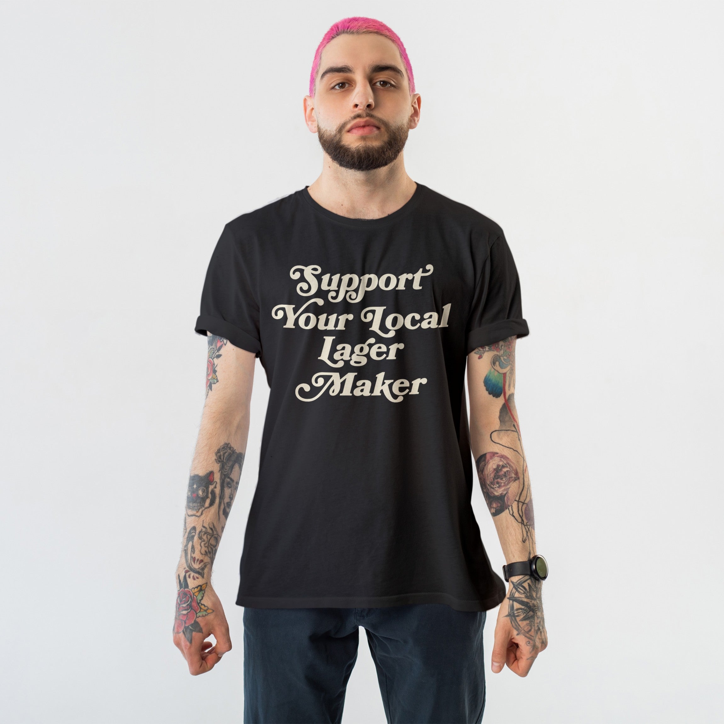Young person with pink hair and tattoos wearing the Support Your Local Lager Maker T-shirt, showcasing their allegiance to local breweries with bold script on a black tee.