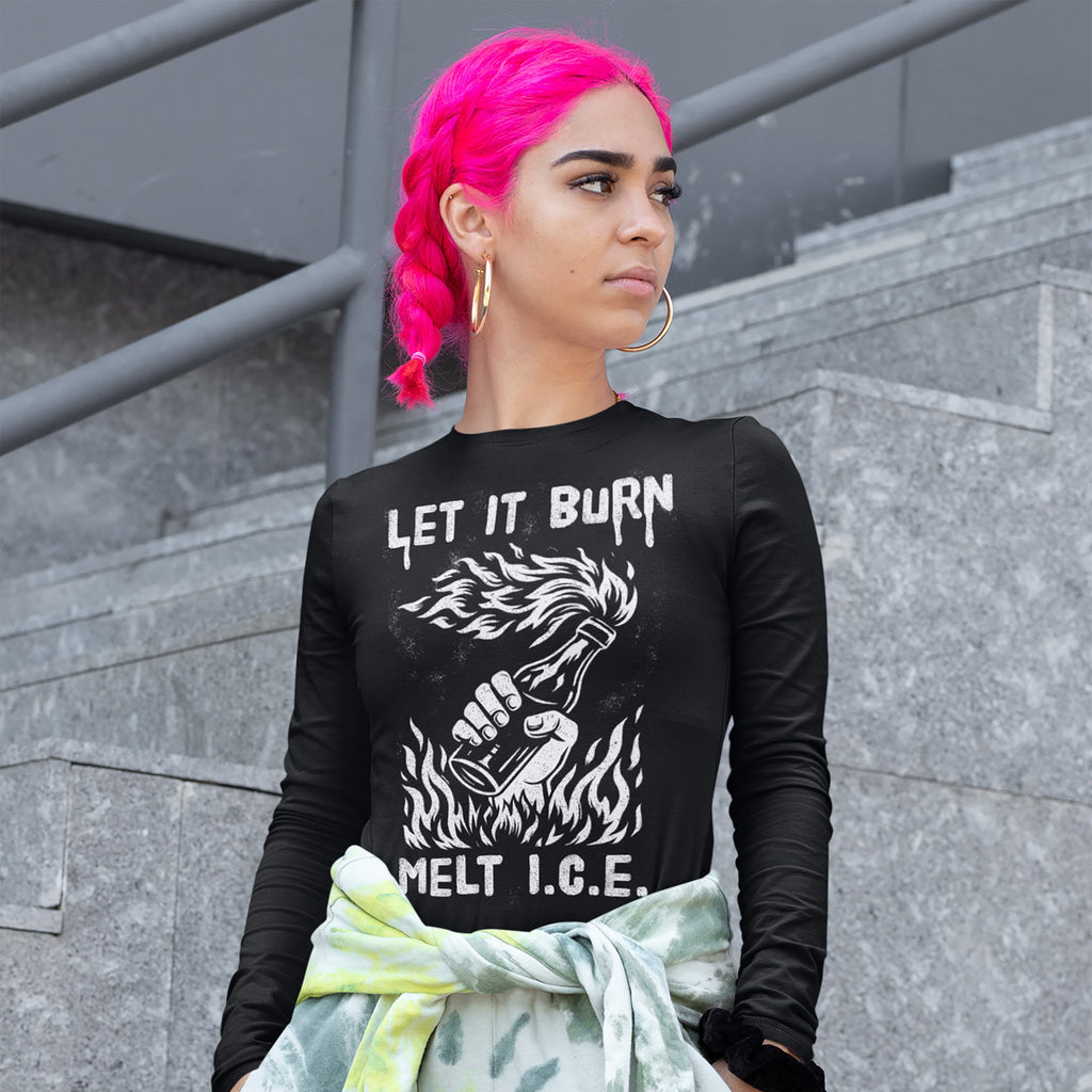 Young person with pink braided hair wears a Let It Burn / Melt ICE long-sleeve shirt featuring a flaming bottle graphic, symbolizing anti-fascist protest, tied with a tie-dye sweatshirt at the waist.