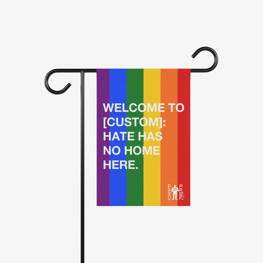 Custom Hate Has No Home Here Pride Garden Flag on a black metal stand, featuring rainbow stripes and white text, promoting inclusivity and equality in outdoor spaces.