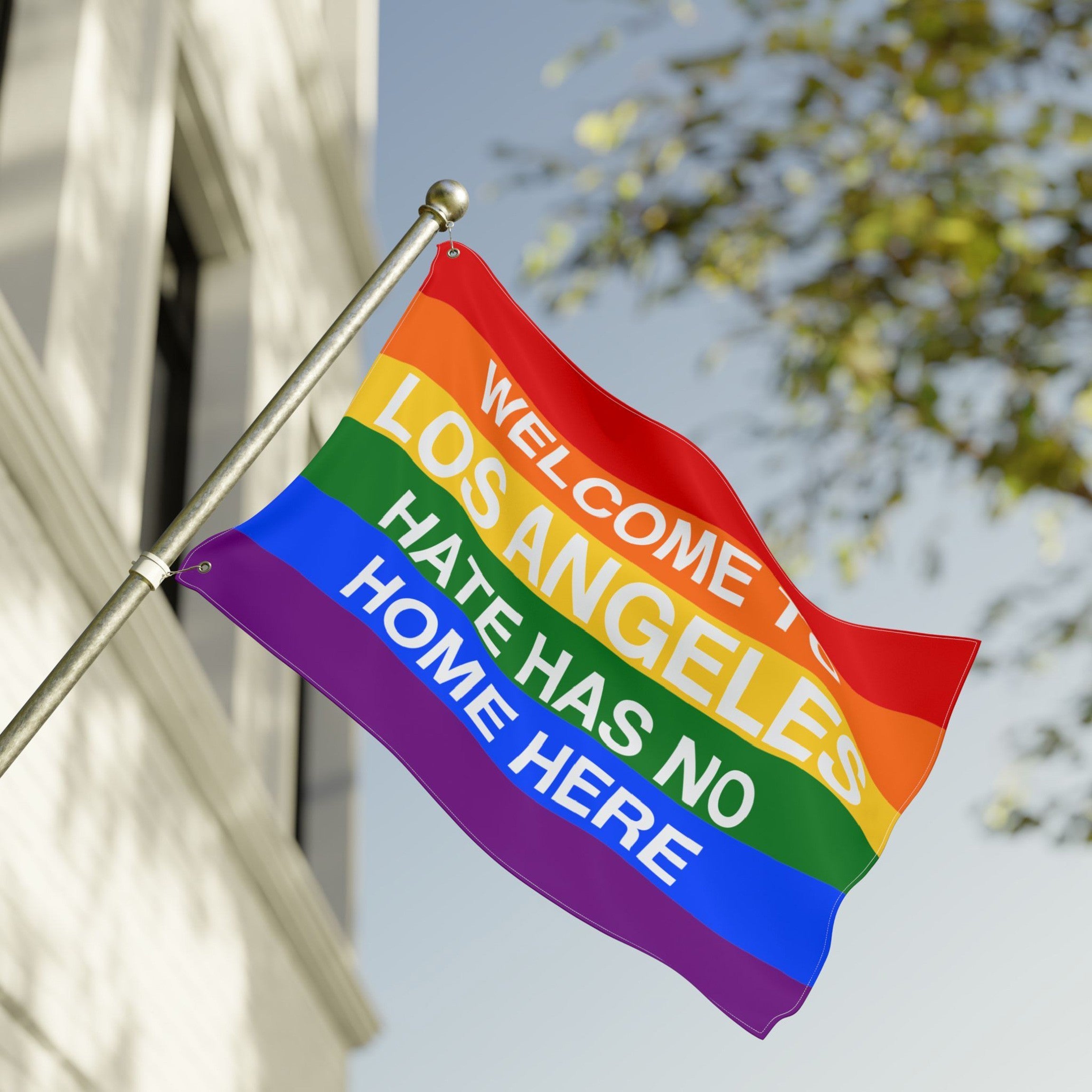 Custom Hate Has No Home Here Pride Flag with bold rainbow stripes and a message promoting unity and inclusivity, mounted on a pole outside a building.