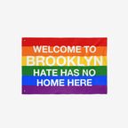 Custom Hate Has No Home Here Pride Flag with bold white lettering on rainbow stripes, featuring metal grommets for hanging. Personalize with your city name to promote love, unity, and inclusion.